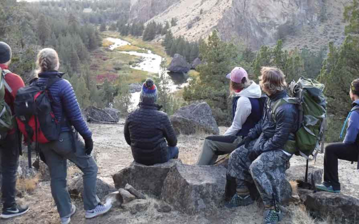 a group of people stand and sit high above a river as they survey it